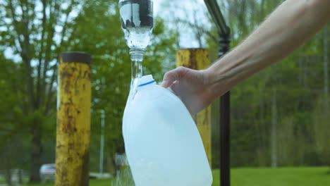una mano masculina asiática joven y firme que sostiene una jarra de plástico para obtener agua de un grifo público