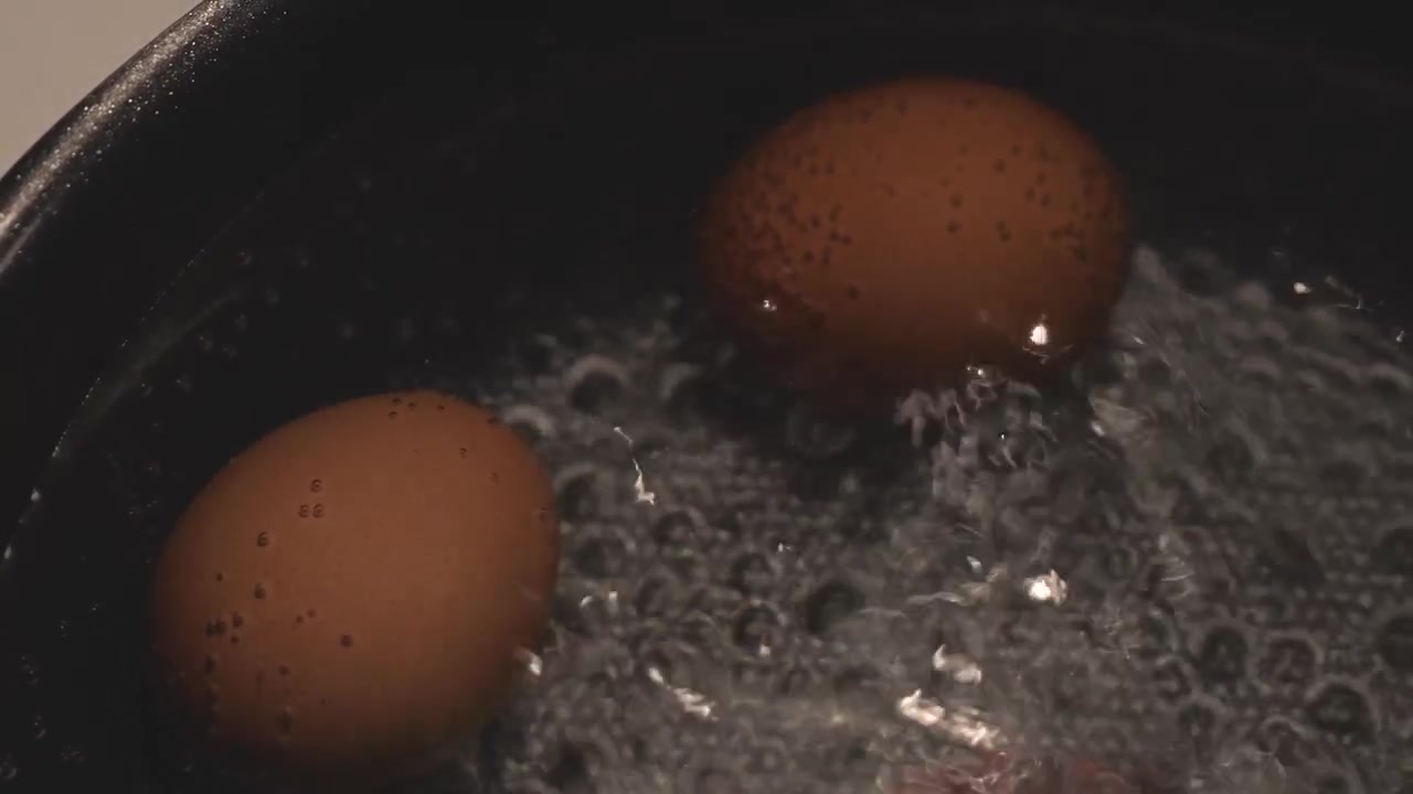 Close-up of boiled eggs cooking in a pot of hot water, capturing steam, gentle bubbling, and a simple everyday food preparation scene.
