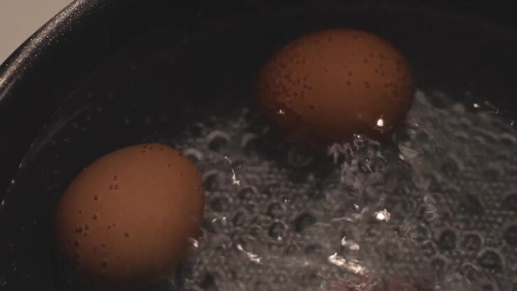 Close-up of boiled eggs cooking in a pot of hot water, capturing steam, gentle bubbling, and a simple everyday food preparation scene.