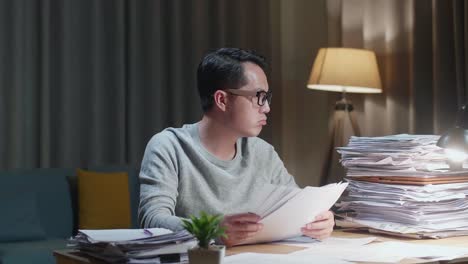 tired asian man shaking his head while working hard with documents at the home