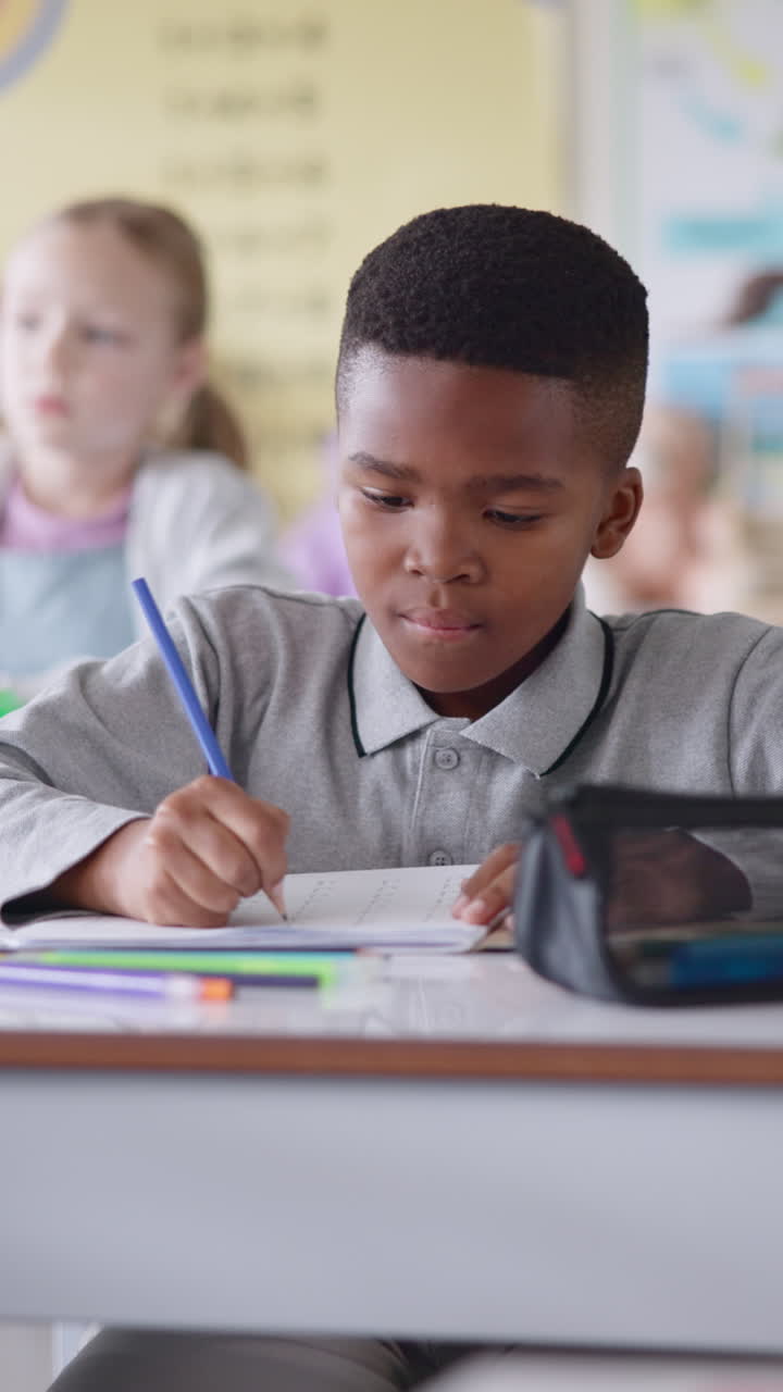 Young boy sitting at a desk in a classroom writing in a notebook