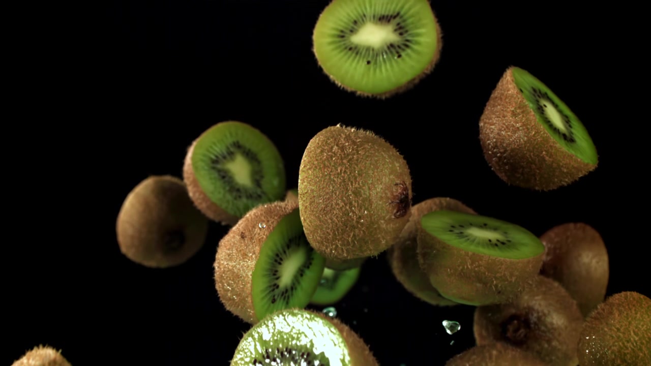 Mitades de kiwi fresco cayendo en cámara lenta con salpicaduras de agua