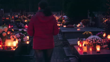 mujer caminando entre las tumbas iluminadas por velas encendidas