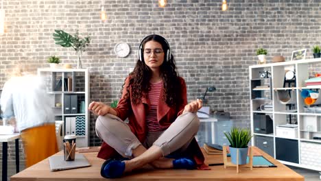 time-lapse of girl listening to music in lotus pose on table wearing headphones