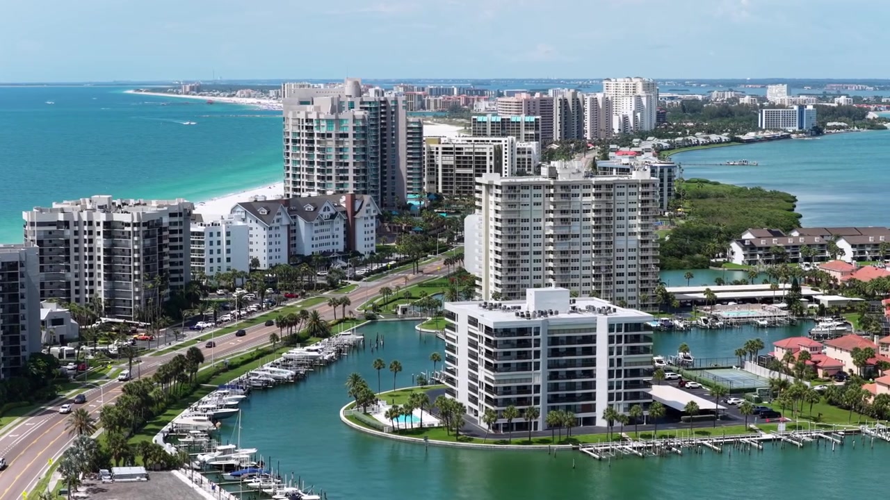 Condominios de lujo de gran altura flanquean el canal y la marina de Clearwater Beach, con aguas turquesas del Golfo y una costa de arena blanca bajo cielos azules en Clearwater Beach, Florida, EE. UU. Vista aérea con dron.