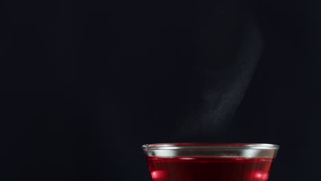 hot red drink in glass with steam on dark background