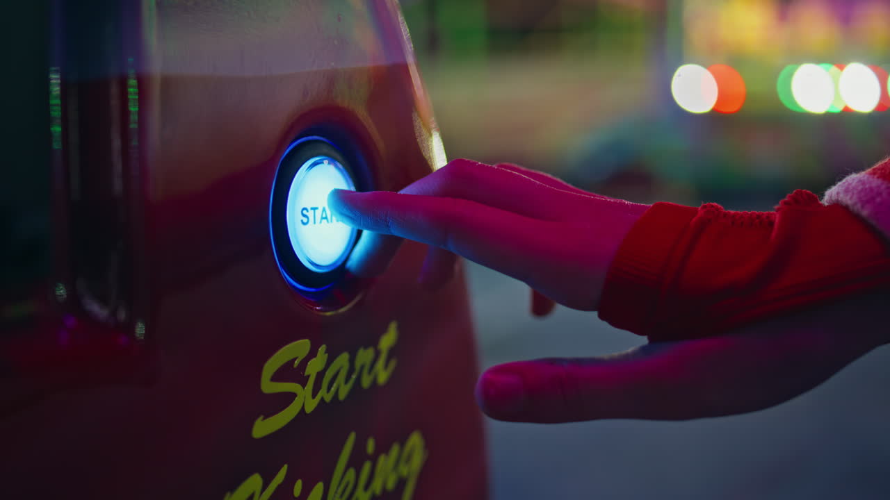 Hand pushing start button at arcade game machine closeup. Girl playing luna park
