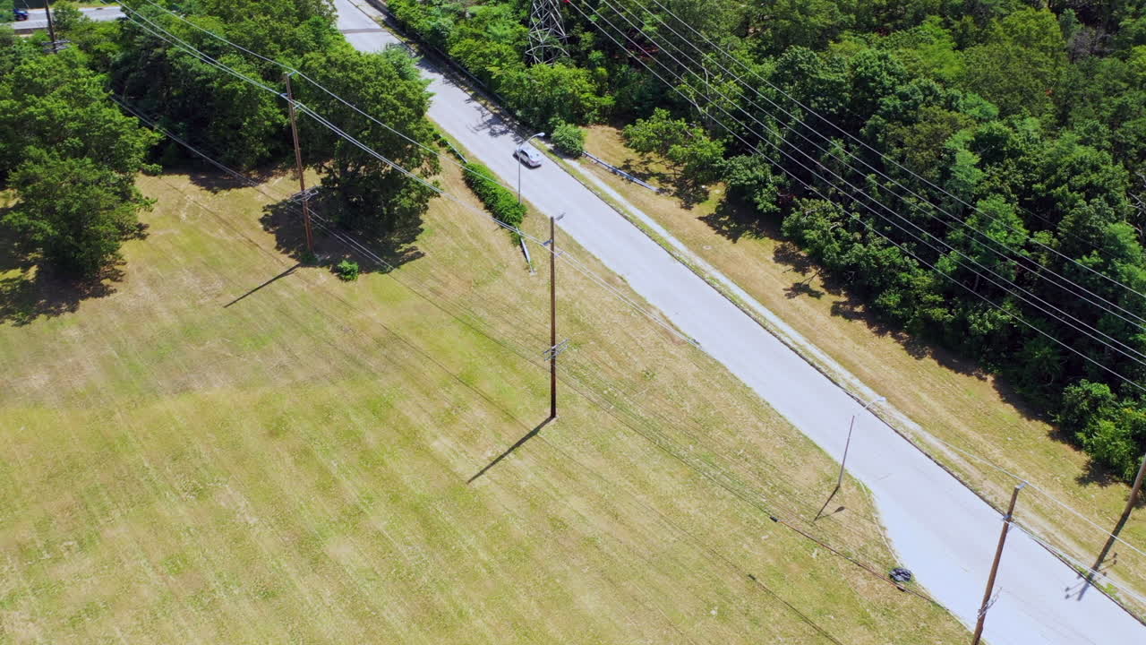 вид с высоты птичьего полета на линии электропередач, зеленое поле - деревья, внизу проезжает белый автомобиль