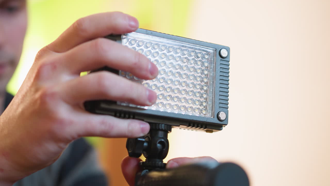 Studio guy adjusting microphone stand, preparing it for setup. Focus on his arm, action of preparing equipment, microphone and camera visible, studio setting with green and orange background