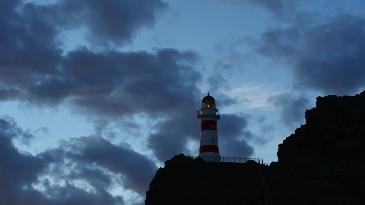 Time lapse of the Lighthouse of Cape Palliser on a Cliff.  on the North Island of New Zealand. Blue hour clouds moving fast. Light of the lighthouse visible
