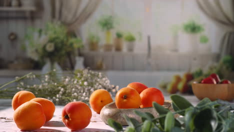 a hand delicately places a ripe apricot into a rustic wooden bowl surrounded by other apricots on a bright kitchen table, with soft floral decor in the background.