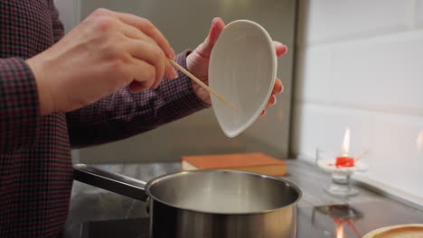 vista lateral de una persona convirtiendo el azúcar en una olla con casi quemado, acción de cocina en la cocina con la estufa encendida, preparando ingredientes para postre o caramelo en la cocina moderna