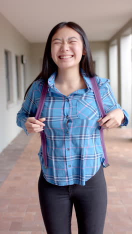 vertical video: in highschool, asian female student wearing blue plaid shirt is laughing