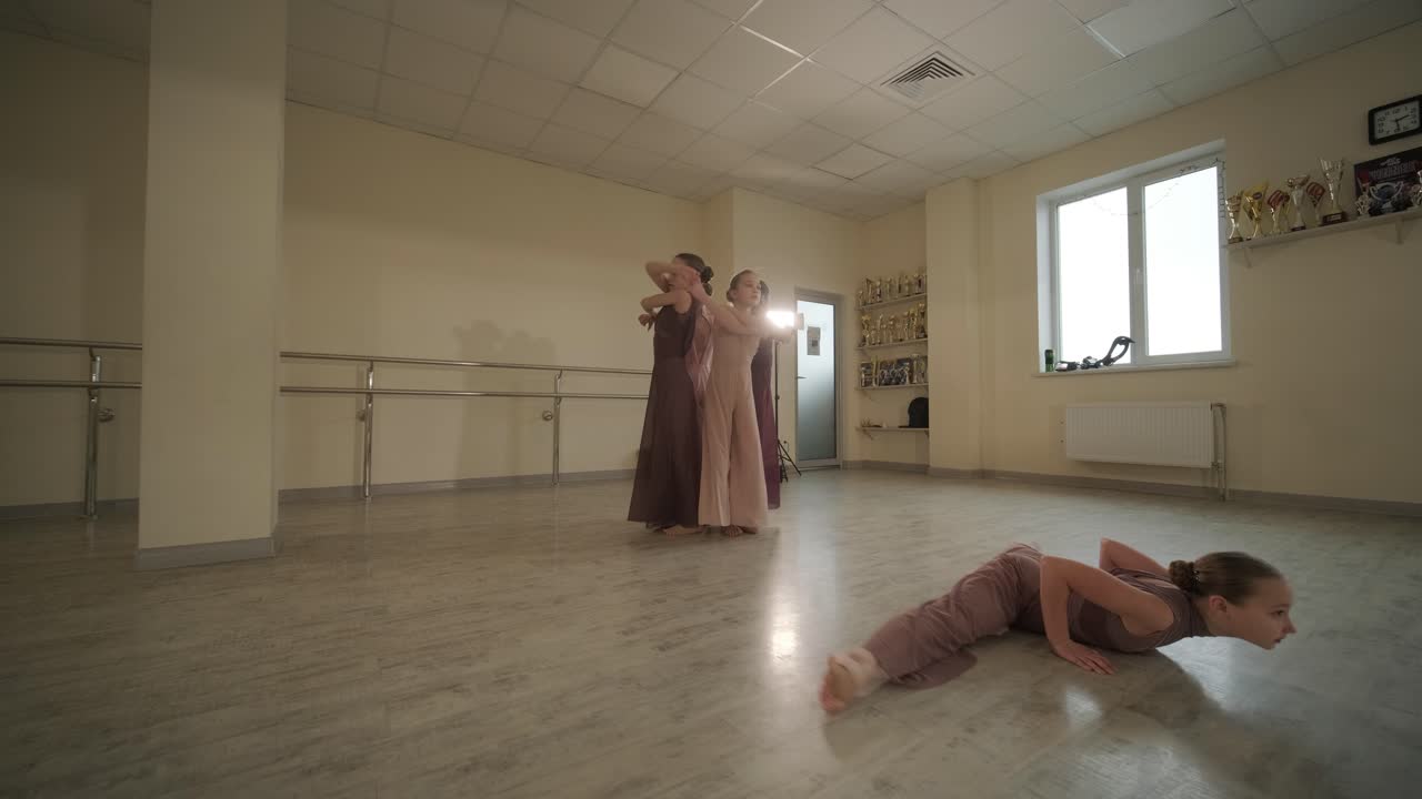 группа молодых студентов балета в черной танцевальной одежде практикует позиции в просторной балетной студии с деревянным полом и настенными решетками. сосредоточенные выражения и синхронизированные движения.