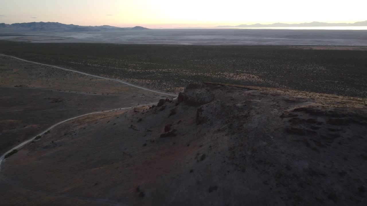 High-angle drone shot of a dusty road cutting through Utah desert terrain at dusk, showcasing warm tones, open plains, and canyon silhouettes