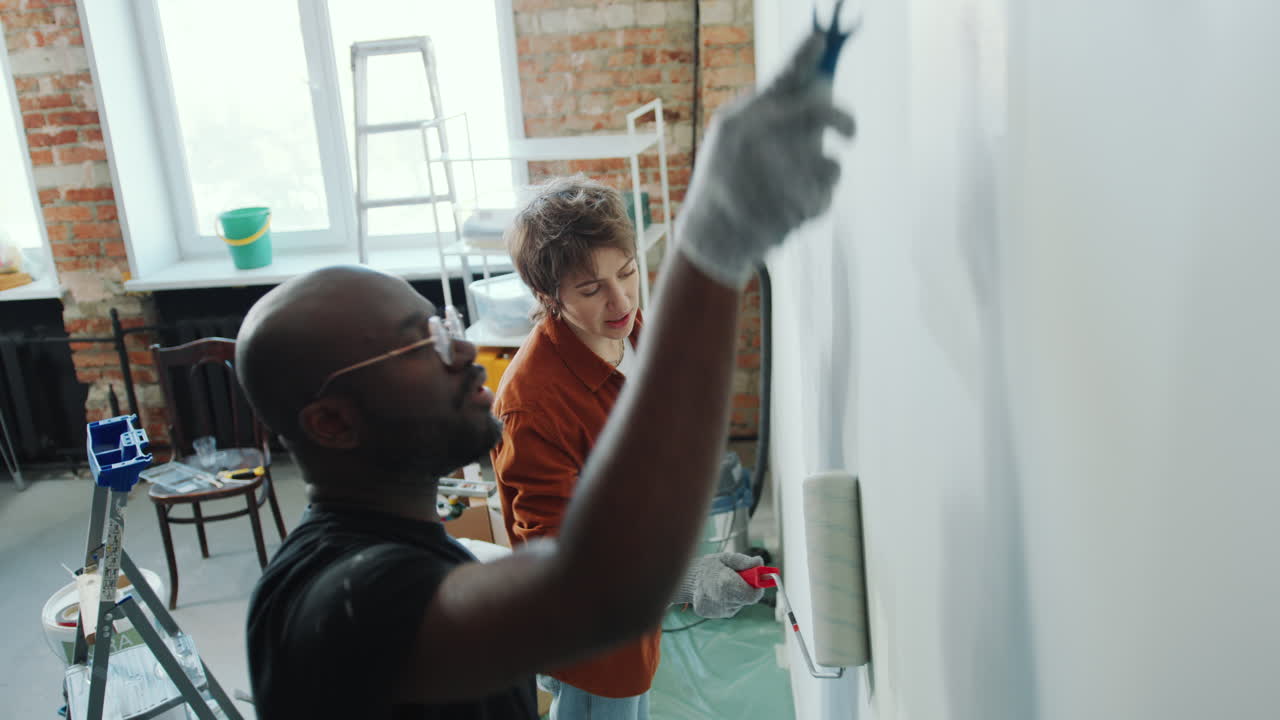 Black Man Painting Walls with Help of Wife during Apartment Renovation