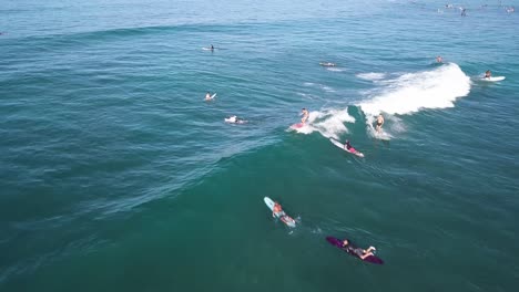 three surfers catching a medium sized wave on waikiki beach in honolulu hawaii on a beautiful day, aerial dolly pullback