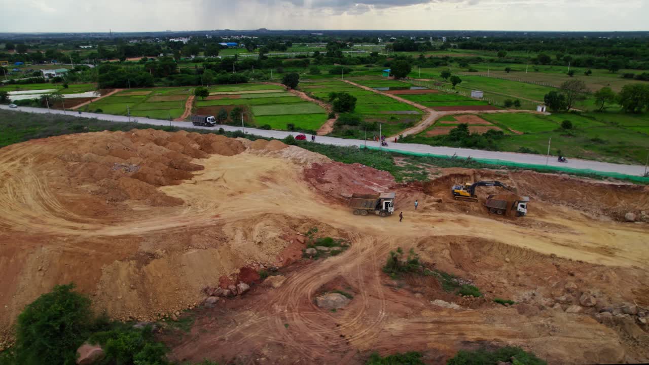 A truck loading sand through Excavators in background crop fields lands with clouds and sky in telangana, india. day time, tilt down, drone shot, 4k