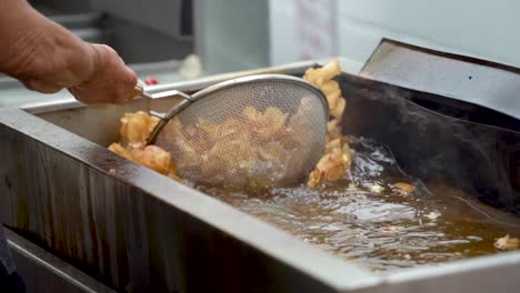 slow motion of using strainer to lift hot curly, tornado fries out of hot oil