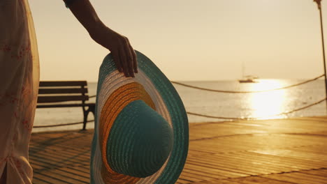 una mujer con un sombrero en la mano camina por el muelle hacia el sol naciente sueño del concepto de viaje constante