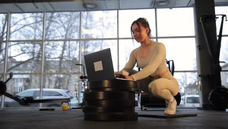 woman in sportswear sits on gym floor using laptop a woman in sportswear is comfortably sitting on the floor in a gym using a laptop computer for leisure the laptop is placed on a white table next to her
