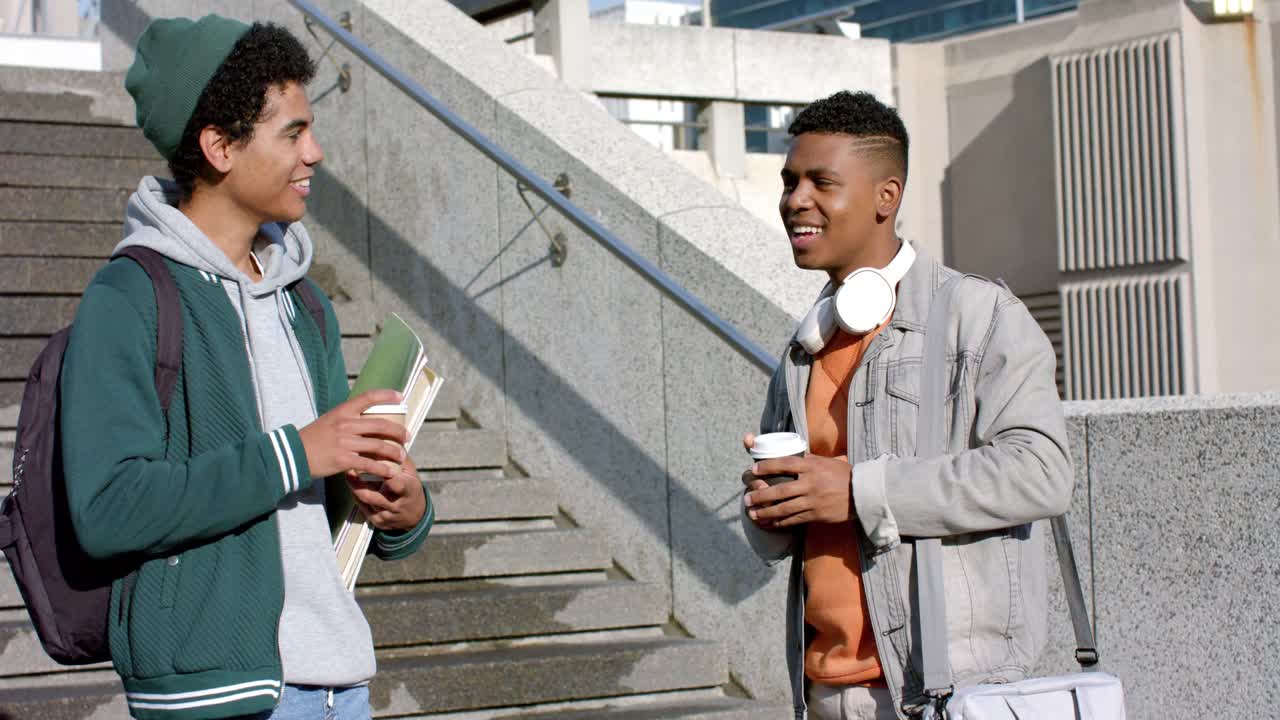 Diverse male students greeting with high-five catching up while sipping coffee on campus stairs