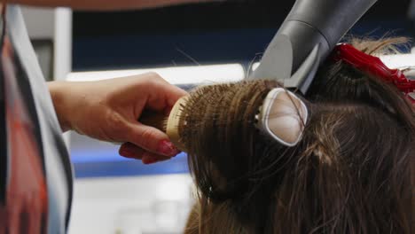 peluquero cepillando el cabello castaño con un cepillo para el cabello mientras se seca el cabello