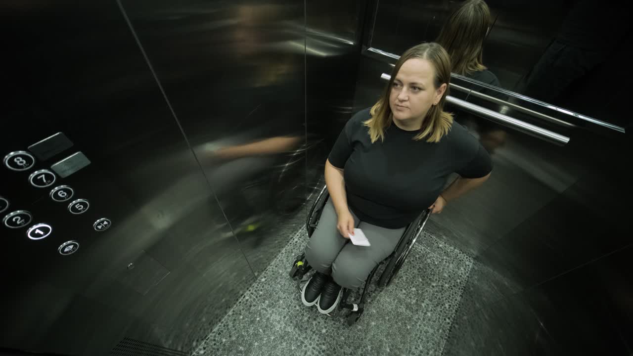 A woman in a wheelchair is inside an elevator, holding an item in her hands, as she waits for the elevator to reach her floor. The image highlights accessibility, independence, and modern infrastructure.