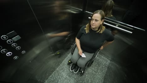 una mujer en silla de ruedas está dentro de un ascensor, sosteniendo un artículo en sus manos, mientras espera que el ascensor llegue a su piso. la imagen destaca la accesibilidad, la independencia y la infraestructura moderna.