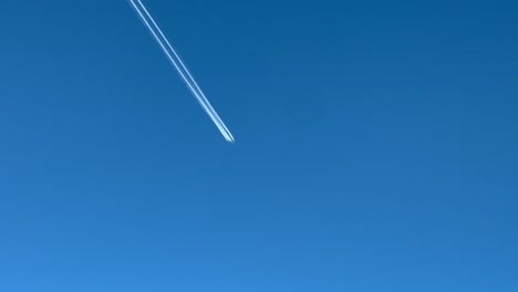 contrail of a huge military 4-engine aircraft crossing a blue sky, shot from an airplane flying bellow