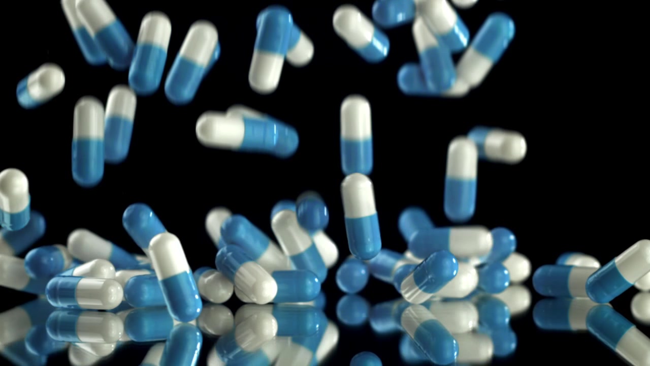 Capsule blu e bianche che cadono al rallentatore su sfondo nero