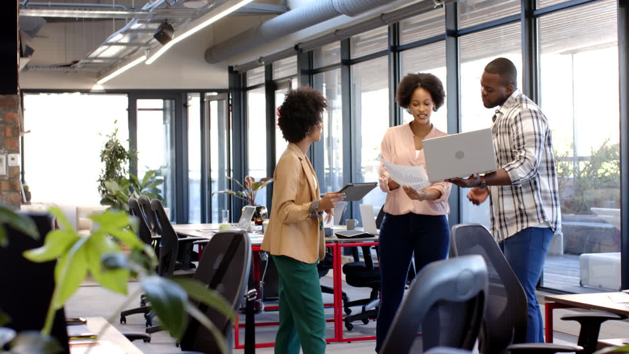 Collègues d'affaires afro-américains discutant de travail avec un ordinateur portable et des graphiques au bureau, avec espace de copie.