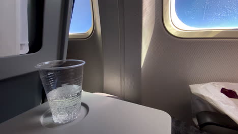 a plastic clear cup of water with gas bubbles on an airplane table