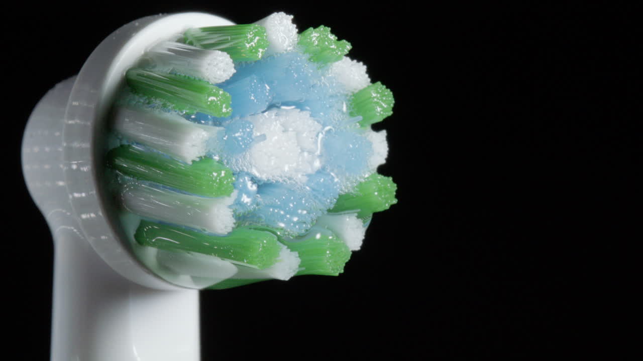 Water droplet in slomo drips from wet electric toothbrush brush head, closeup