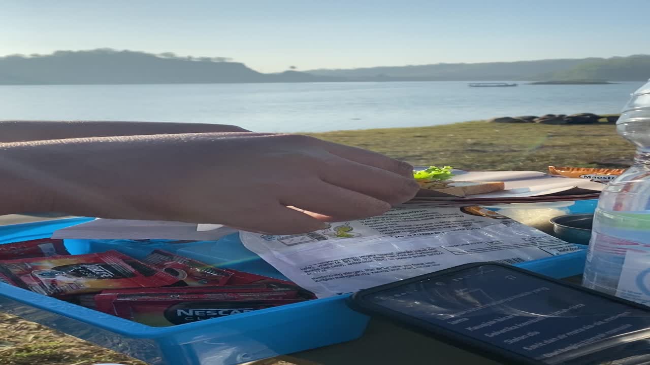 vertical footage, with friends camping and making breakfast of bread, sandwiches, sausages with a view of the clean Sermo reservoir.