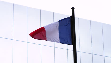 Imágenes-En-Cámara-Lenta-De-La-Bandera-Francesa-Moviéndose-Con-La-Brisa-Con-Un-Edificio-Reflejado-En-El-Fondo