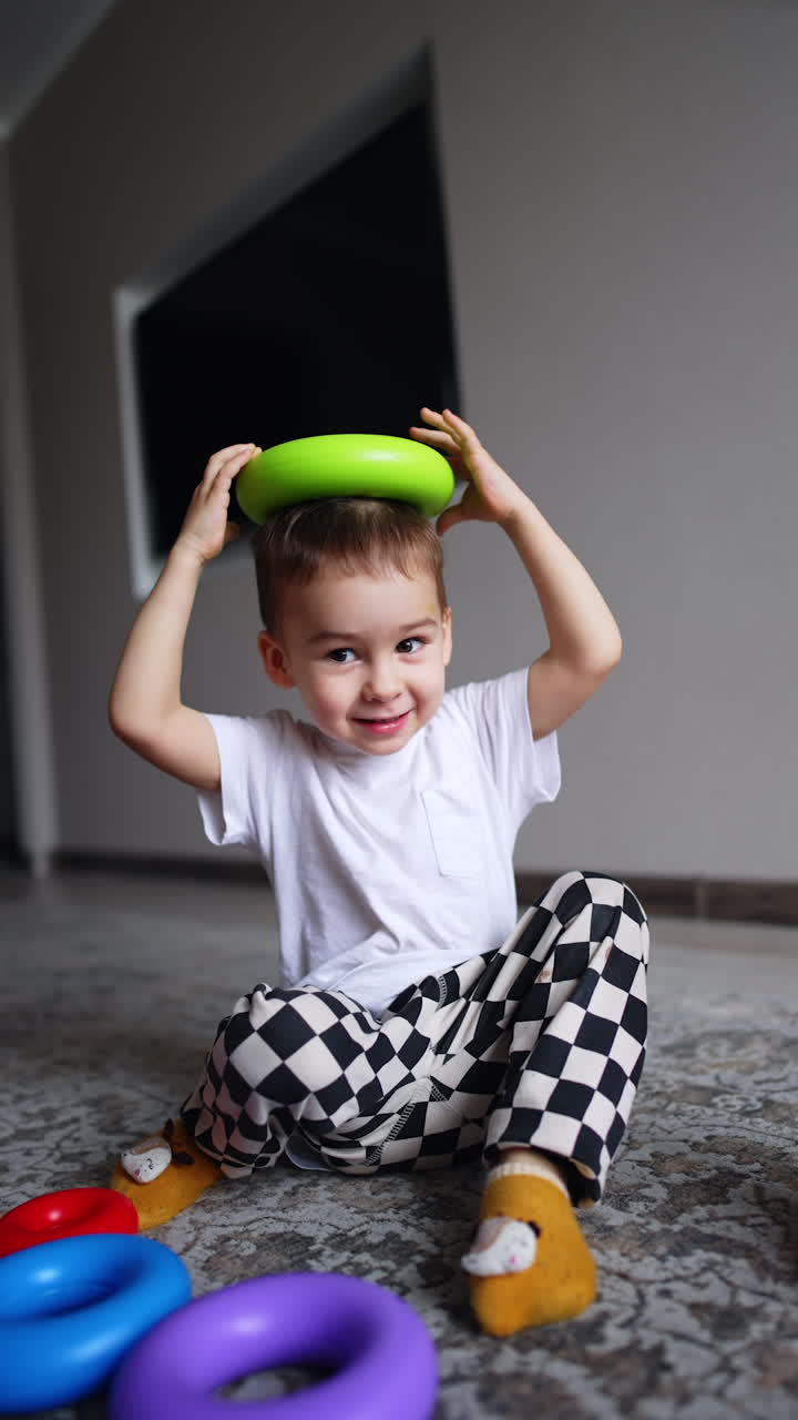 Caucasian toddler plays with pyramid details on the floor. Cute kid takes one ring and puts it on his head. Vertical video.