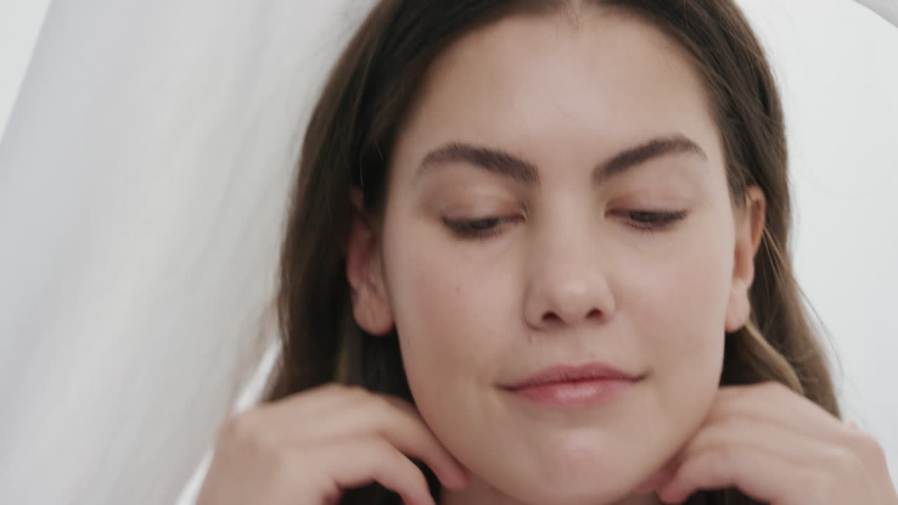 가까운 초상화 아름다운 젊은 여성이 부드러운 건강한 피부를 만지고 손으로 얼굴을 만지고 부드러운 자연 피부를 즐기고 시트 사이에  ⁇ 색 바탕에 여성적인 아름다움