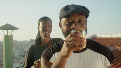 front view of cheerful bearded gay clinking glasses and dancing at camera while his boyfriend is behind him