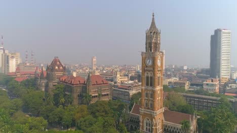 Drone-shot-of-the-Rajabai-Clock-Tower-next-to-the-Bombay-High-Court-Building-and-Oval-Maidan,-an-ornate-1878-clock-tower-modeled-after-Big-Ben-and-featuring-stained-glass-windows-and-musical-chimes