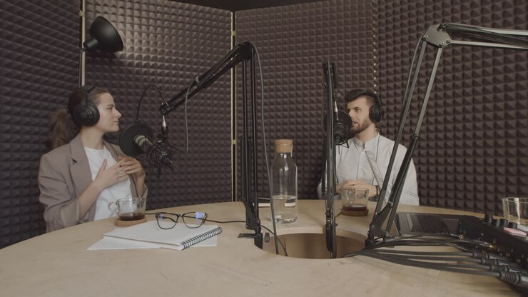 Una giovane donna elegante con la coda di cavallo e un giovane uomo affascinante conversano in uno studio di registrazione radiofonico.