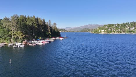 Hermoso-Azul-Día-Soleado-Lago-Punta-De-Flecha-California-Con-Vista-Al-Muelle-Y-Barcos-Acelerando-A-Través-De-La-Escena-Elevación-Aérea-Dolly