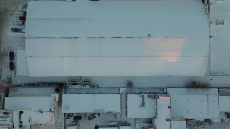 Snow-covered-factory-hall-with-parking-trucks-in-winter