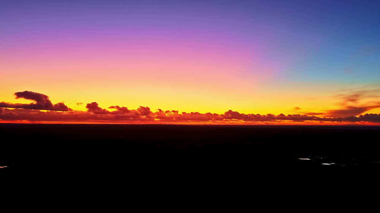Vibrant gradient sunset sky with fiery orange, pink, and blue over dark landscape