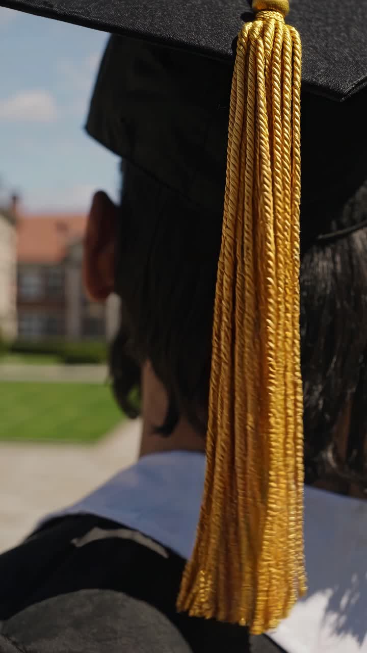 Close-up video shot from behind of a graduate in cap and gown, focusing on the tassel