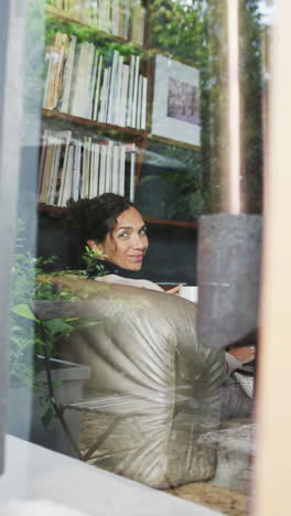 vertical video of biracial woman lying on sofa and looking out window at home, slow motion
