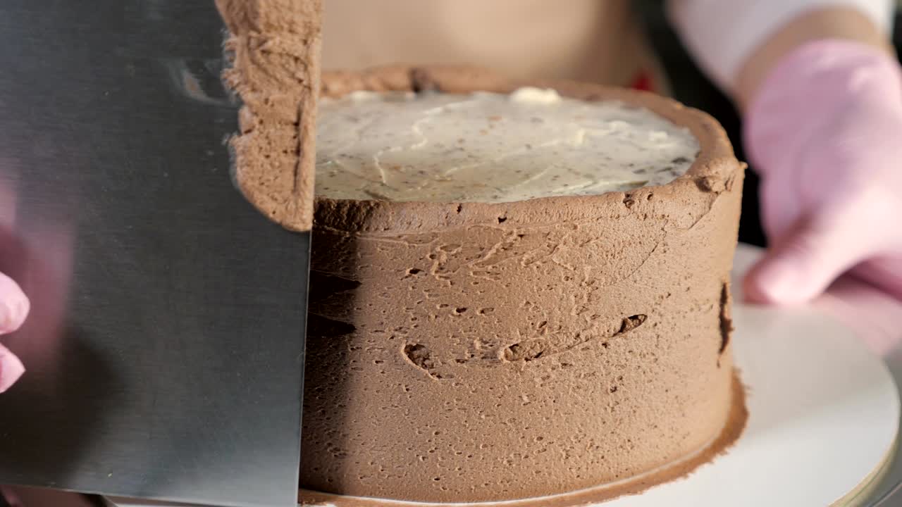 Una pasticcera sta spalmando crema al cioccolato su un pan di Spagna