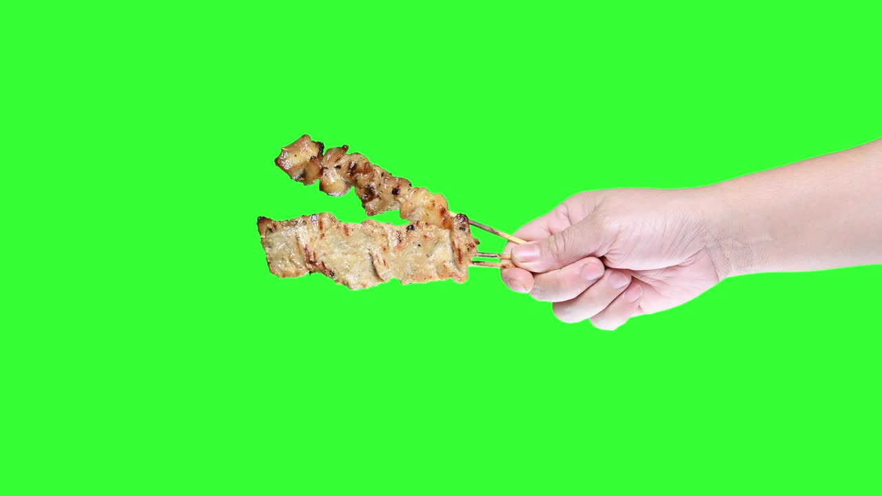 초록색 스크린 배경에 바베큐 사타이 을 들고 있는 손.