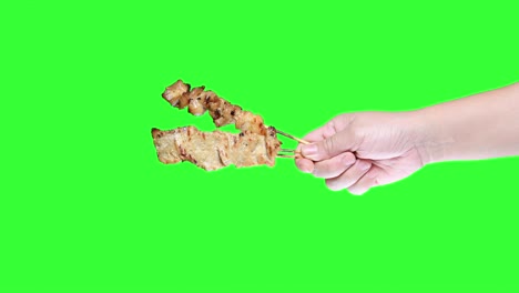 mano sosteniendo pollo satay a la parrilla en el fondo de la pantalla verde.