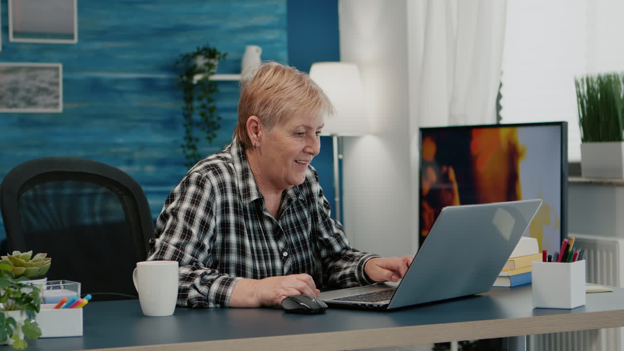 집 에서 일 하는 노인 여자 가 노트북 으로 좋은 소식 을 듣고 있다
